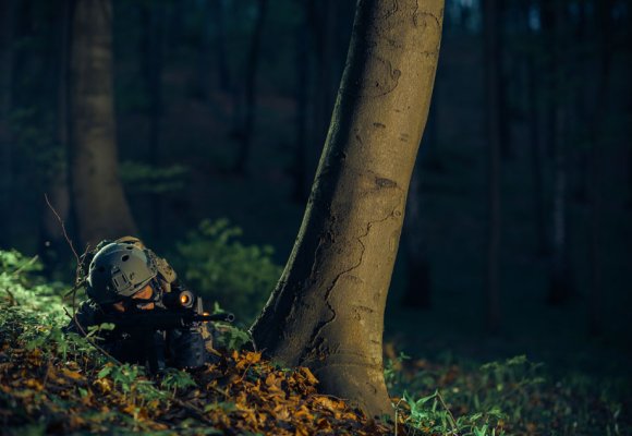 Soldat som ligger med våpen i skogen