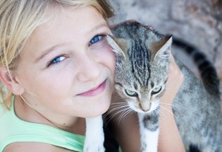 Nærbilde av en jente som holder en katt, hun holder katten inntil kinnet og ser i kamera.